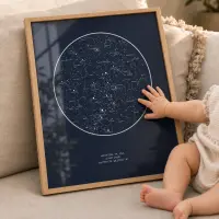 A baby reaching out to touch a light wood framed navy star map print propped on a sofa